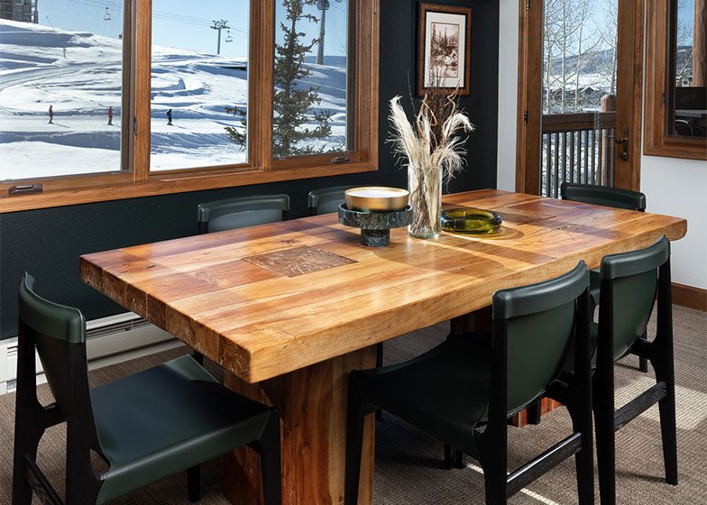 Dining room with a wooden table and six chairs, set near a window with a snowy mountain view outside.